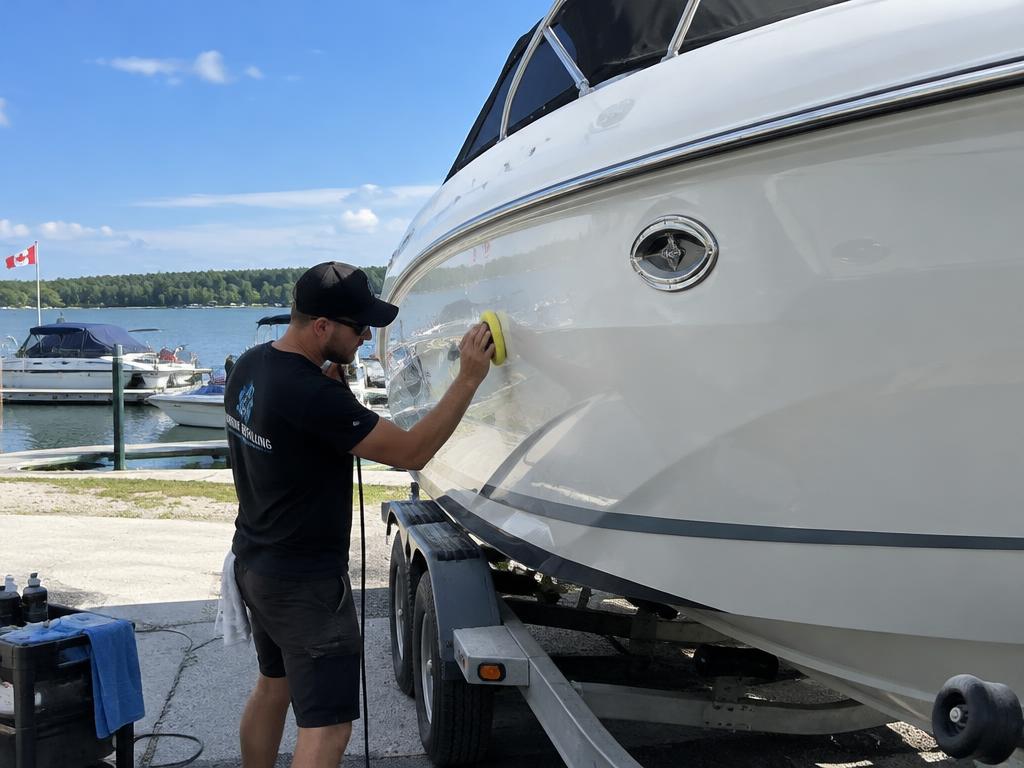 Detailer hand-waxing the hull of a white boat on a trailer