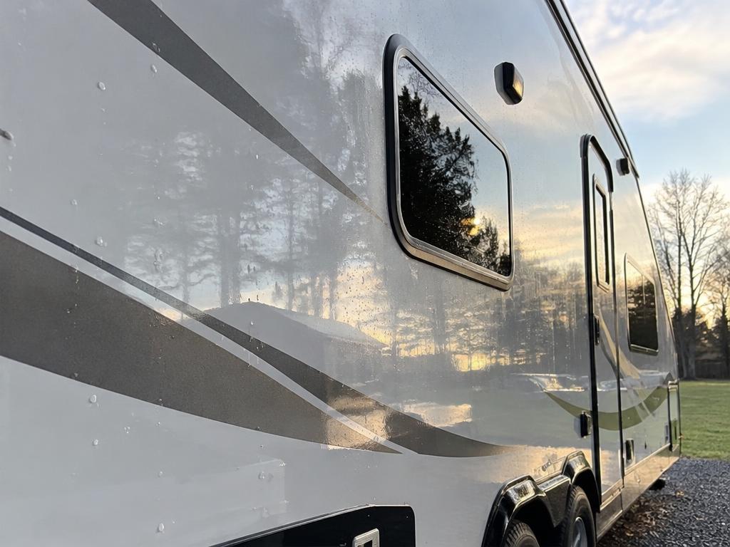 Glossy side of a travel trailer reflecting trees